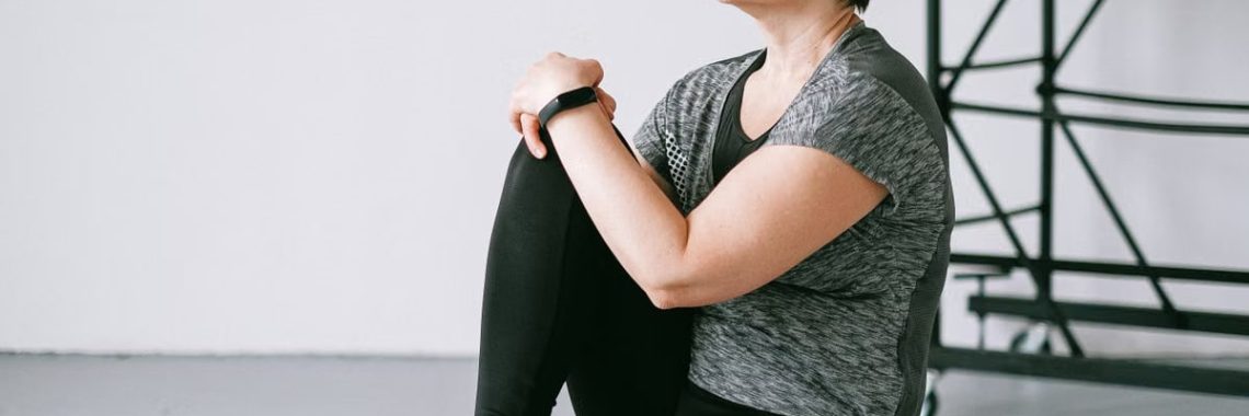 Senior woman in active wear sitting on a wooden box indoors, reflecting on wellness.